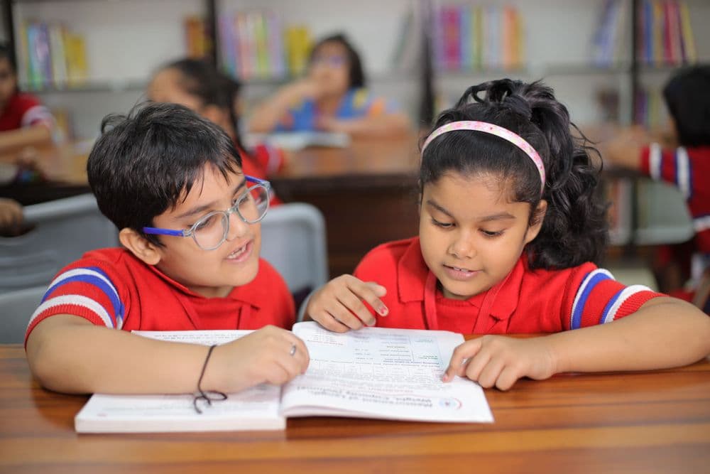 Two children reading a textbook together in a classroom